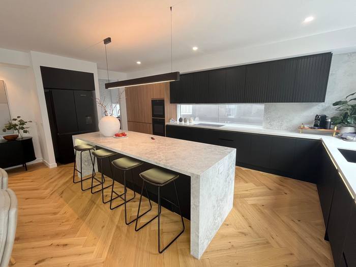 Black kitchen with marble waterfall island and herringbone floor